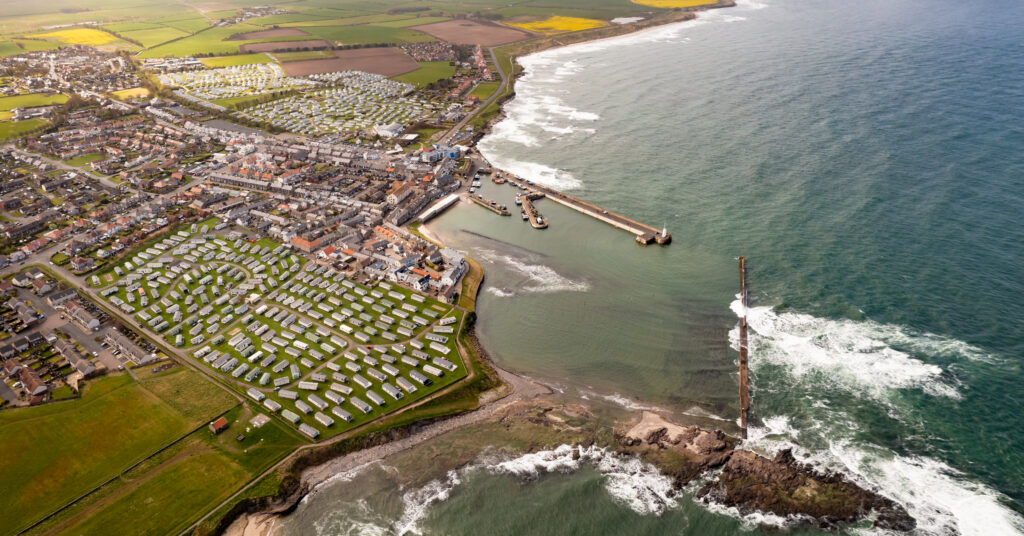 Aerial view of a coastal holiday park with static caravans, village, and harbour overlooking the sea. pressure on the holiday park industry