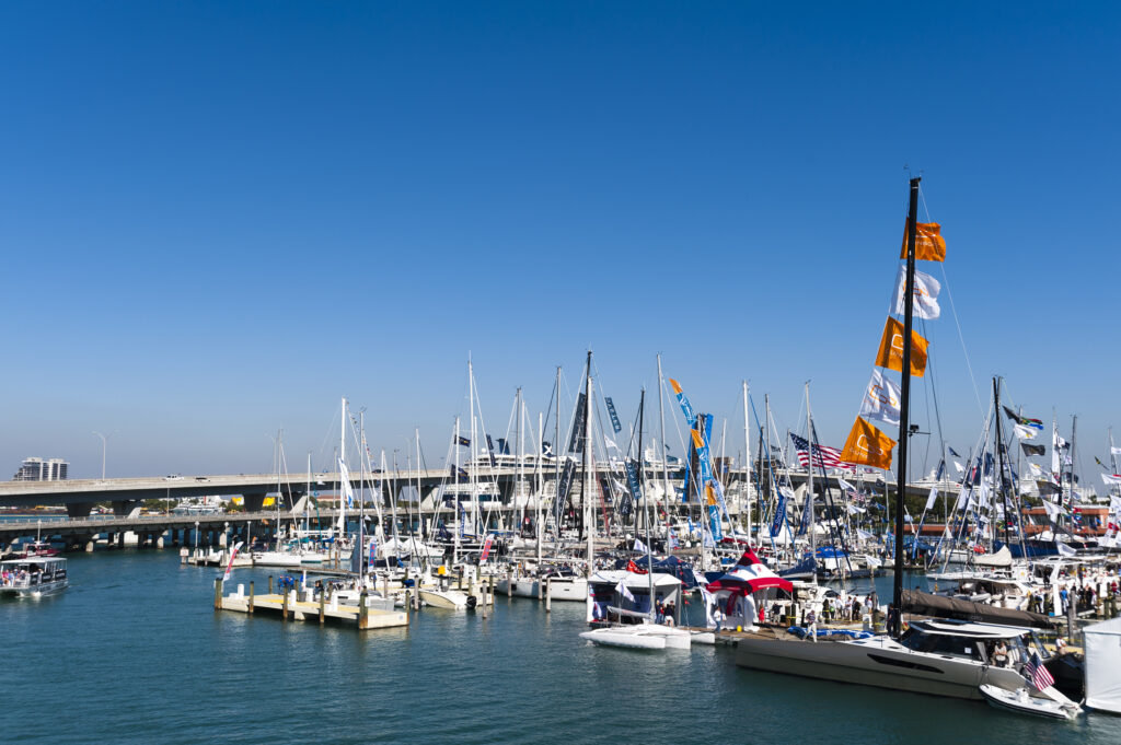Boat show at a marina with yachts, sailboats, and colourful flags under a clear blue sky.