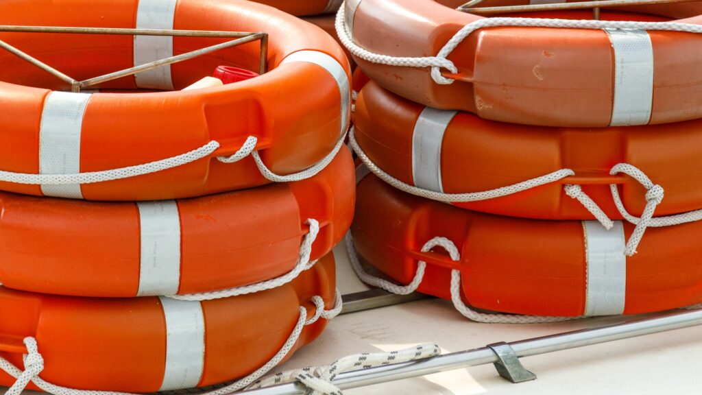 Stack of orange lifebuoys with white straps and ropes, symbolising marina safety and regulations. health and safety in the marine industry