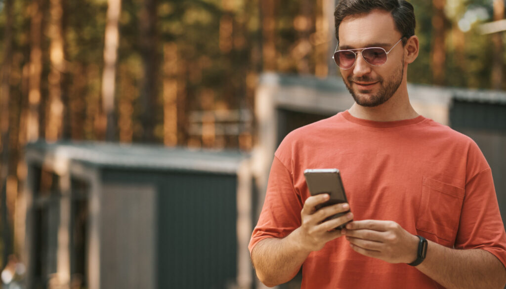Man outdoors smiling while using a smartphone, representing mobile apps for holiday parks guests